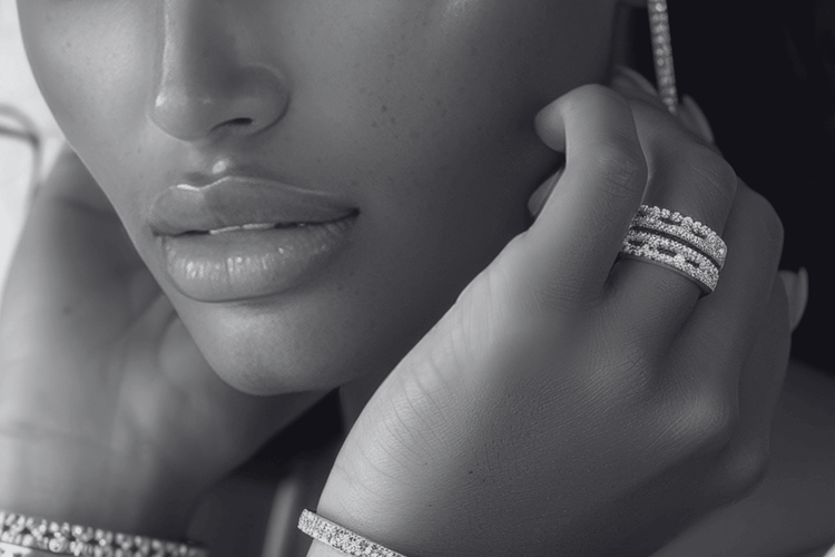 Close-up of a person wearing multiple diamond rings on fingers and an earring.